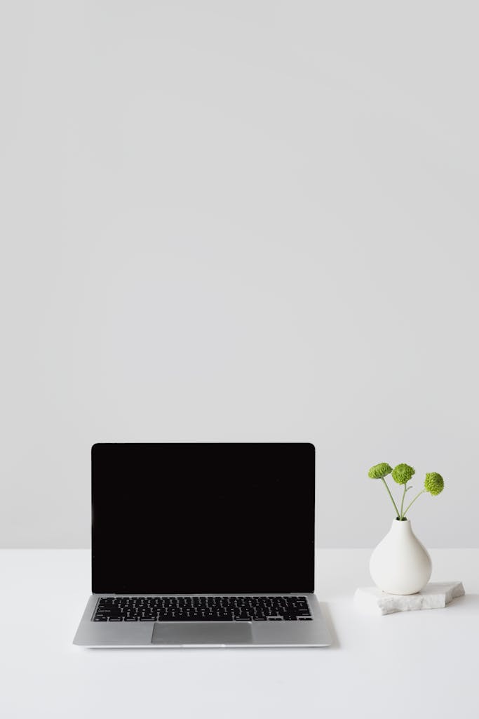 Clean and minimalistic office setup featuring a laptop and vase on a white desk.